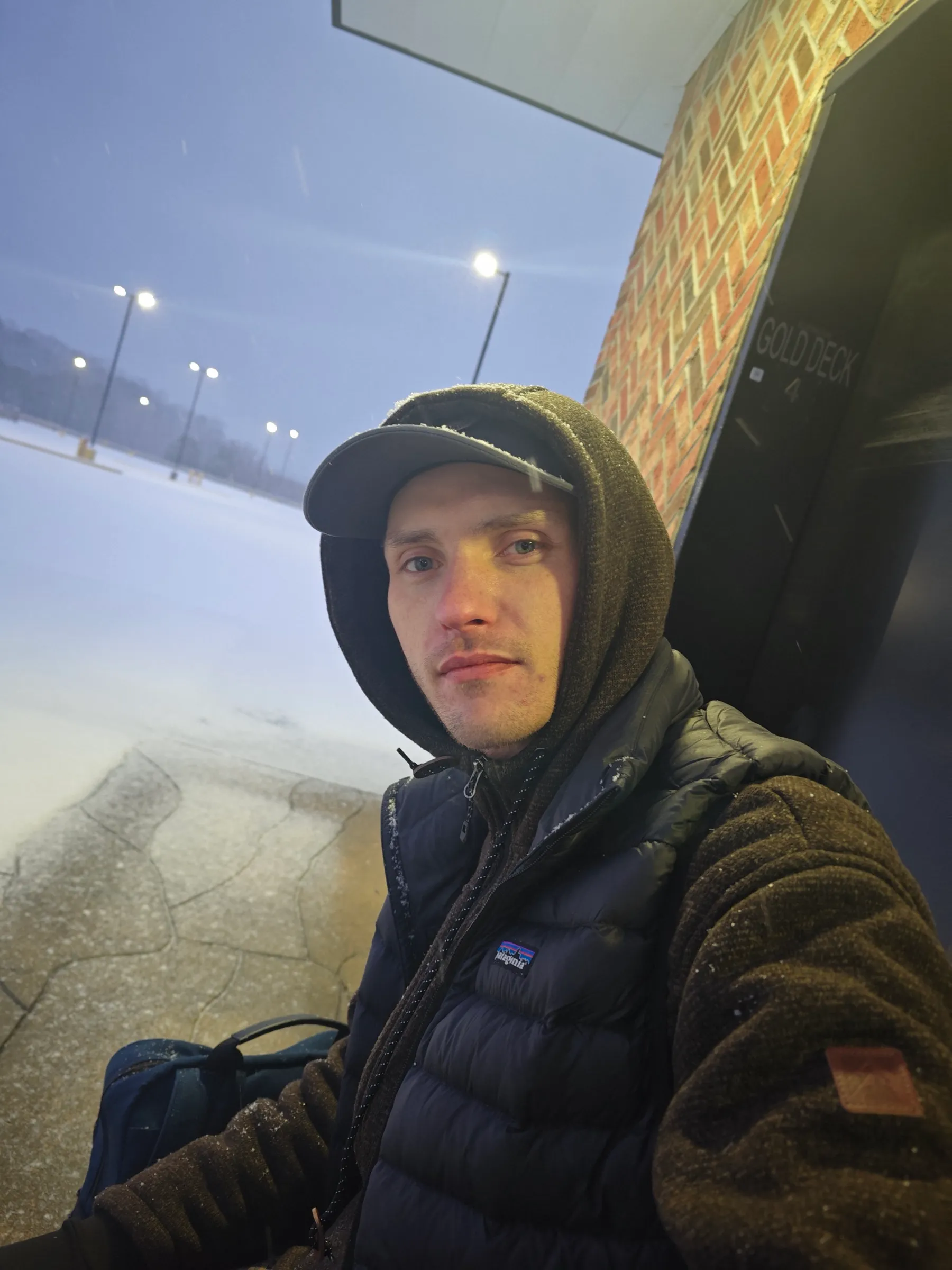 The author at the Gold Deck 4 elevator of the emptied mall — hood up, snow falling, the white parking deck stretching out behind.